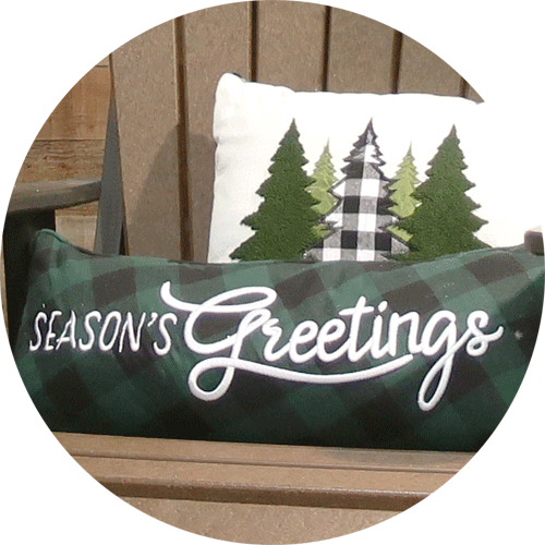 A long, green plaid pillow that says Season's Greetings, with another pillow with green trees behind it.